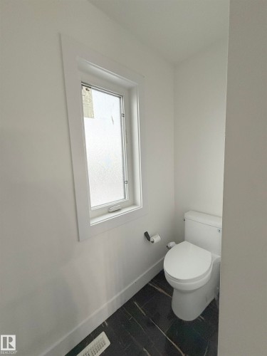 Powder room featuring a white single-hung window with privacy glass, a contemporary toilet, and dark stone-look tile flooring - 1210 Peregrine Terrace, Edmonton, AB - Indoor Photo Showing Bathroom