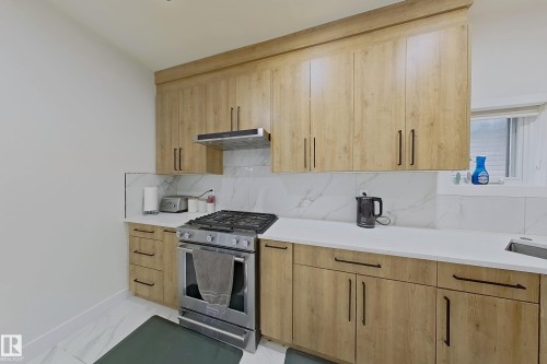 Modern kitchen featuring wood-finish cabinetry with black hardware, white countertops, and a white marble-look backsplash - 1210 Peregrine Terrace, Edmonton, AB - Indoor Photo Showing Kitchen