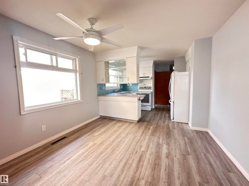 Open-concept living space featuring wood-finish flooring, a contemporary ceiling fan, and a kitchen with white cabinetry, a light-colored countertop, and a blue tile backsplash - 11131 52 Street, Edmonton, AB - Indoor