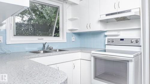 Kitchen featuring white cabinetry, light speckled countertops, and a blue tiled backsplash - 11131 52 Street, Edmonton, AB - Indoor Photo Showing Kitchen With Double Sink