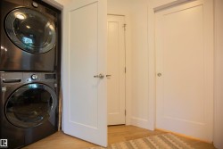 Stackable washer and dryer unit with modern panel doors and wood-finish flooring - 