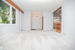 Carpeted living area featuring light gray walls, large windows with white trim, and a built-in wooden shelving unit - 
