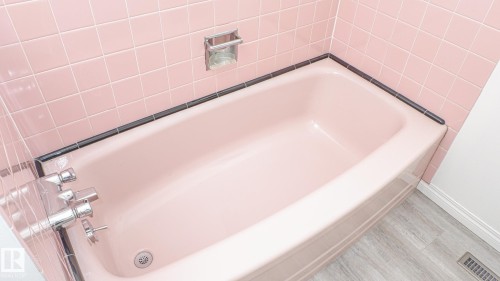 Bathtub with pink subway tile surround, dark tile trim, chrome fixtures, and wood-finish flooring - 11131 52 Street, Edmonton, AB - Indoor Photo Showing Bathroom
