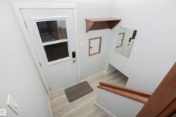 Entryway with light wood-finish flooring, white paneled door with upper glass panel, and contrasting wood staircase - 