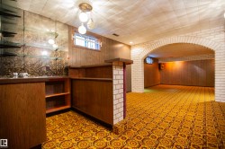 Finished basement with an arched brick entryway, wood-paneled walls, and a built-in bar featuring glass shelving and a patterned accent wall - 