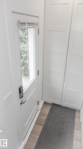 Entryway featuring a white paneled door with glass insert, wood-finish flooring, and built-in white cabinetry - 11131 52 Street, Edmonton, AB - Indoor Photo Showing Other Room