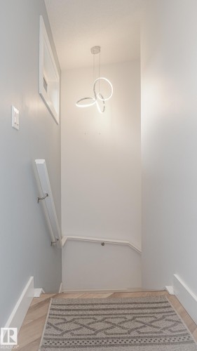 Modern pendant light fixture illuminating a stairwell with light wood-finish flooring - 11131 52 Street, Edmonton, AB - Indoor