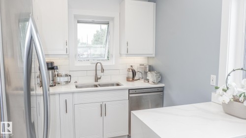 Kitchen featuring white shaker cabinetry, stainless steel appliances, a double basin sink, subway tile backsplash, and light-toned countertops - 11131 52 Street, Edmonton, AB - Indoor Photo Showing Kitchen With Double Sink