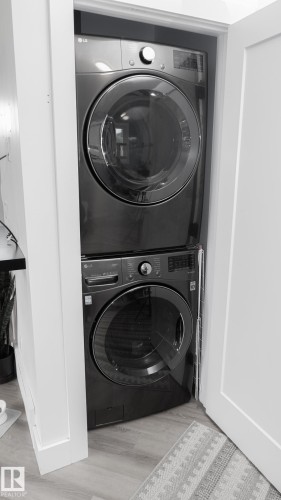 Stacked laundry appliances within a dedicated closet space, featuring a dark finish and front-loading design - 11131 52 Street, Edmonton, AB - Indoor Photo Showing Laundry Room