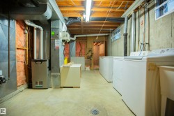 Utility area featuring concrete flooring, exposed ceiling joists, multiple laundry appliances, and a visible furnace unit - 