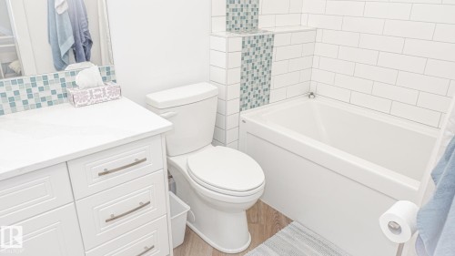 Modern bathroom featuring a white vanity with integrated sink, subway tile accents, patterned mosaic tile, a white toilet, and a built-in bathtub - 11131 52 Street, Edmonton, AB - Indoor Photo Showing Bathroom