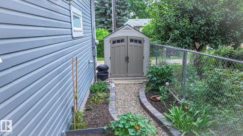 Exterior featuring grey horizontal siding, a gravel pathway with paver edging, a built-in storage shed, and a chain-link fence - 11131 52 Street, Edmonton, AB - Outdoor