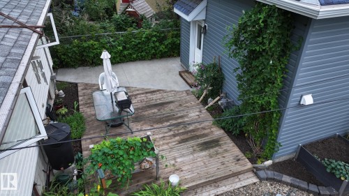 Expansive outdoor deck featuring wood-finish planks, a concrete patio area, mature landscaping, and an adjacent building with horizontal siding - 11131 52 Street, Edmonton, AB - Outdoor With Deck Patio Veranda With Exterior