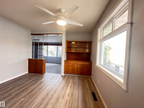 Spacious interior featuring wood-finish flooring, a contemporary ceiling fan, and a built-in wooden hutch with glass-front cabinets - 11131 52 Street, Edmonton, AB - Indoor Photo Showing Other Room
