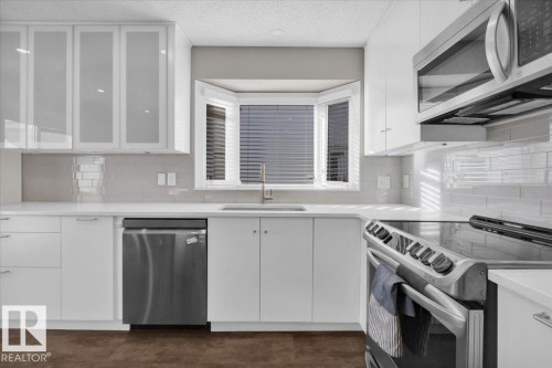 Kitchen with stainless steel appliances, white cabinetry, glass insert cabinets, decorative backsplash, and a textured ceiling - 3515 20 Avenue, Edmonton, AB - Indoor Photo Showing Kitchen