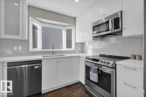 Kitchen featuring appliances with stainless steel finishes, white cabinetry, a textured ceiling, backsplash, and light stone countertops - 3515 20 Avenue, Edmonton, AB - Indoor Photo Showing Kitchen With Stainless Steel Kitchen With Upgraded Kitchen