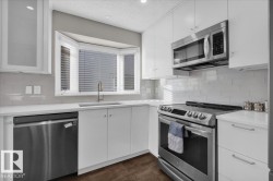 Kitchen featuring appliances with stainless steel finishes, white cabinetry, a textured ceiling, backsplash, and light stone countertops - 