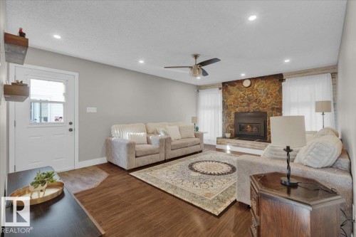 Living area featuring plenty of natural light, a textured ceiling, wood finished floors, a stone fireplace, and recessed lighting - 3515 20 Avenue, Edmonton, AB - Indoor Photo Showing Living Room With Fireplace