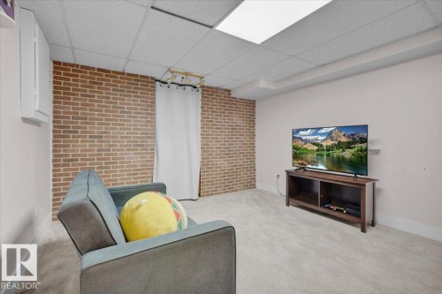 Carpeted living area featuring a paneled ceiling and brick wall - 3515 20 Avenue, Edmonton, AB - Indoor