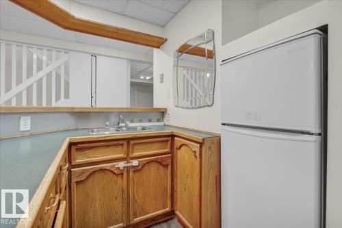 Kitchen with freestanding refrigerator, light countertops, brown cabinetry, and a paneled ceiling - 3515 20 Avenue, Edmonton, AB - Indoor Photo Showing Kitchen With Double Sink