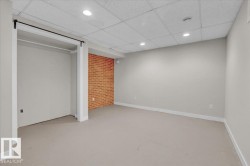 Unfurnished bedroom featuring a paneled ceiling, concrete flooring, a closet, recessed lighting, and brick wall - 