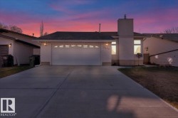 View of front of home with a chimney, driveway, a garage, stucco siding, and a yard - 