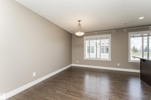 Spacious room featuring wood-finish flooring, two large windows, a central pendant light fixture, and recessed ceiling lighting - 110 3625 144 Avenue, Edmonton, AB - Indoor Photo Showing Other Room