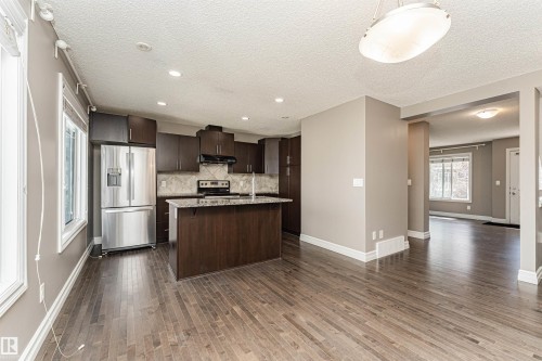 Open-concept kitchen featuring dark wood cabinetry, stainless steel appliances, a center island with a sink, and pendant lighting - 110 3625 144 Avenue, Edmonton, AB - Indoor Photo Showing Kitchen
