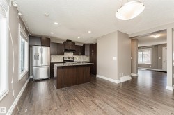 Open-concept kitchen featuring dark wood cabinetry, stainless steel appliances, a center island with a sink, and pendant lighting - 