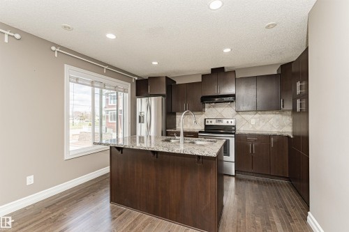 Kitchen featuring a central island with an undermount sink, granite countertops, and dark wood-finish cabinetry - 110 3625 144 Avenue, Edmonton, AB - Indoor Photo Showing Kitchen With Double Sink With Upgraded Kitchen