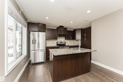 Kitchen featuring dark wood-finish cabinetry, stainless steel appliances, granite countertops, and wood-finish flooring - 110 3625 144 Avenue, Edmonton, AB - Indoor Photo Showing Kitchen
