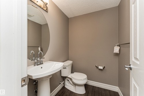Pedestal sink with chrome fixtures, oval mirror, and wall-mounted light fixture - 110 3625 144 Avenue, Edmonton, AB - Indoor Photo Showing Bathroom