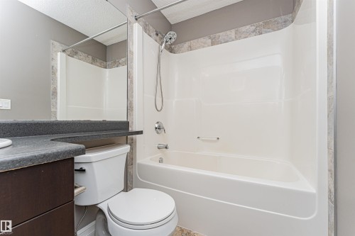 White bathtub and shower combination with a stone-finish tile surround, chrome fixtures, and a curved shower rod - 110 3625 144 Avenue, Edmonton, AB - Indoor Photo Showing Bathroom