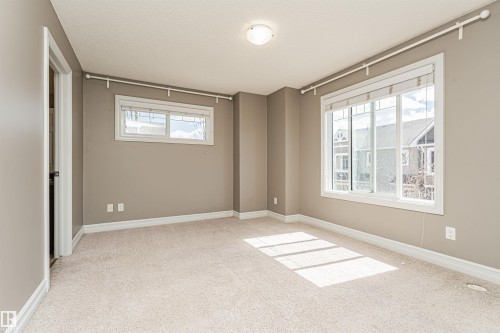 Neutral-toned room featuring light-colored carpeting, white trim, and two windows with white frames - 110 3625 144 Avenue, Edmonton, AB - Indoor Photo Showing Other Room