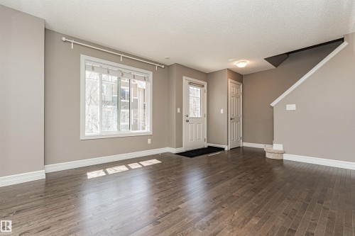 Open concept living area featuring dark wood-finish flooring, a large window with white trim, and neutral paint - 110 3625 144 Avenue, Edmonton, AB - Indoor Photo Showing Other Room
