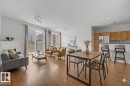 Open-concept living space featuring wood-finish flooring, a white mantelpiece, and sliding glass doors to a balcony - 411 10033 110 Street, Edmonton, AB  - Indoor 