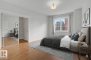 Bedroom featuring wood-finish flooring, a window with city buildings visible, mirrored sliding closet doors, and a ceiling-mounted light fixture - 411 10033 110 Street, Edmonton, AB  - Indoor Photo Showing Bedroom 