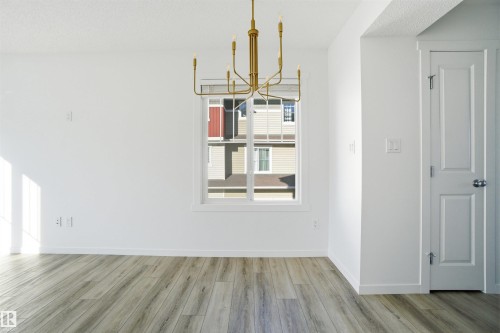 Bright interior space featuring a multi-light brass chandelier, white walls, and wood-finish flooring - 64 17832 78 Street, Edmonton, AB - Indoor Photo Showing Other Room