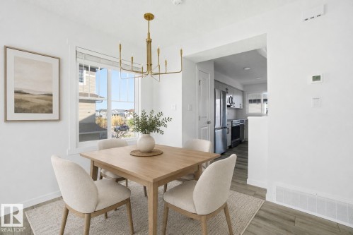 Dining area featuring a modern brass chandelier, large window, and wood-finish flooring - 64 17832 78 Street, Edmonton, AB - Indoor Photo Showing Dining Room