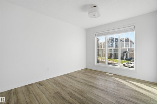 Spacious room featuring wood-finish flooring and a large picture window with blinds - 64 17832 78 Street, Edmonton, AB - Indoor Photo Showing Other Room