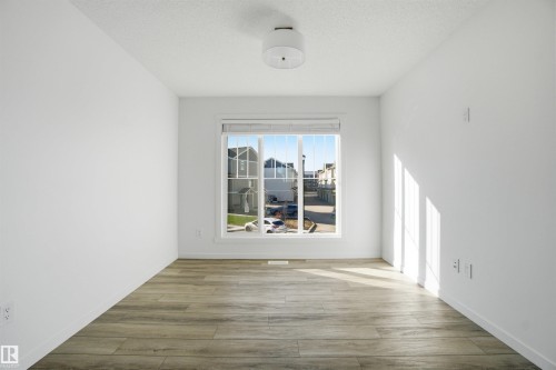 Bright interior space featuring a large window with white blinds, wood-finish flooring, white baseboards, and a contemporary ceiling light fixture - 64 17832 78 Street, Edmonton, AB - Indoor Photo Showing Other Room