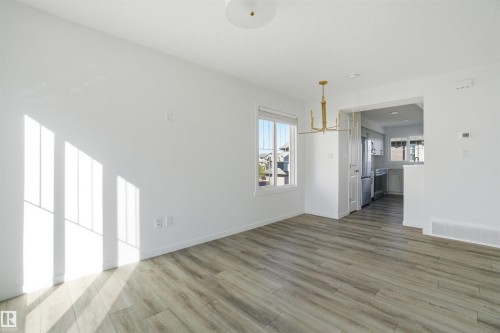 Bright interior space featuring light wood-finish flooring, a contemporary gold-tone chandelier, and a large window - 64 17832 78 Street, Edmonton, AB - Indoor Photo Showing Other Room