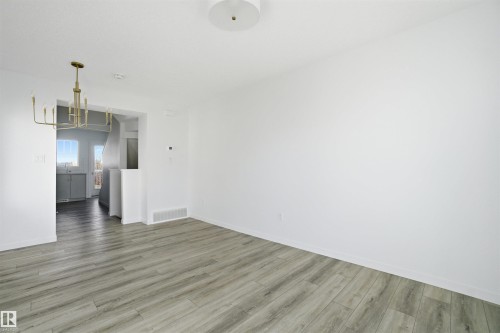 Open concept living space featuring neutral gray wood-finish flooring, a modern brass chandelier, white painted walls, and a ceiling-mounted light fixture - 64 17832 78 Street, Edmonton, AB - Indoor Photo Showing Other Room