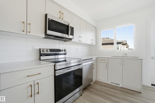 Modern kitchen featuring stainless steel appliances, white subway tile backsplash, light wood-finish flooring, and light-toned cabinetry with gold-tone hardware - 64 17832 78 Street, Edmonton, AB - Indoor Photo Showing Kitchen