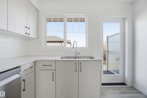 Contemporary kitchen featuring white cabinetry, a double basin stainless steel sink with a high-arc faucet, and light-toned countertops - 64 17832 78 Street, Edmonton, AB - Indoor Photo Showing Kitchen With Double Sink