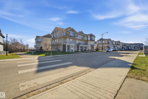 Streetscape featuring multi-story properties with light-toned siding and dark-trimmed windows - 64 17832 78 Street, Edmonton, AB - Outdoor