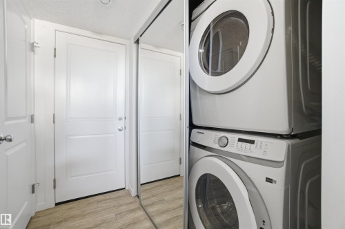 Stackable washer and dryer unit, wood-finish flooring, white paneled doors, and full-length mirrored closet doors - 64 17832 78 Street, Edmonton, AB - Indoor Photo Showing Laundry Room