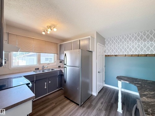 Kitchen featuring stainless steel refrigerator, white tile backsplash, a double basin sink, and wood-finish flooring - 3912 108 Street, Edmonton, AB - Indoor Photo Showing Kitchen With Double Sink