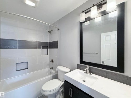 Bathroom featuring a white bathtub with light gray and dark gray tiled surround, two built-in shower niches, and a showerhead with a curved shower rod - 3912 108 Street, Edmonton, AB - Indoor Photo Showing Bathroom
