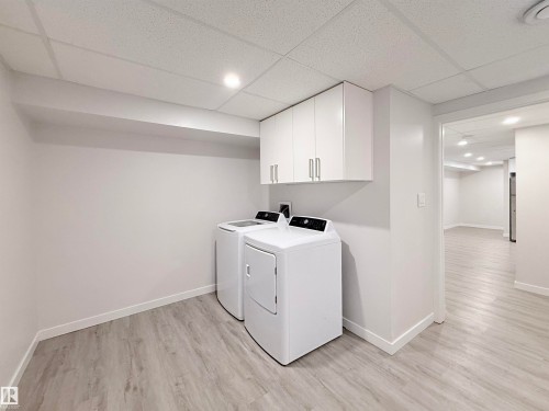 Dedicated laundry area featuring a drop ceiling, light wood-finish flooring, white wall cabinetry with brushed nickel hardware, and recessed lighting - 3912 108 Street, Edmonton, AB - Indoor Photo Showing Laundry Room
